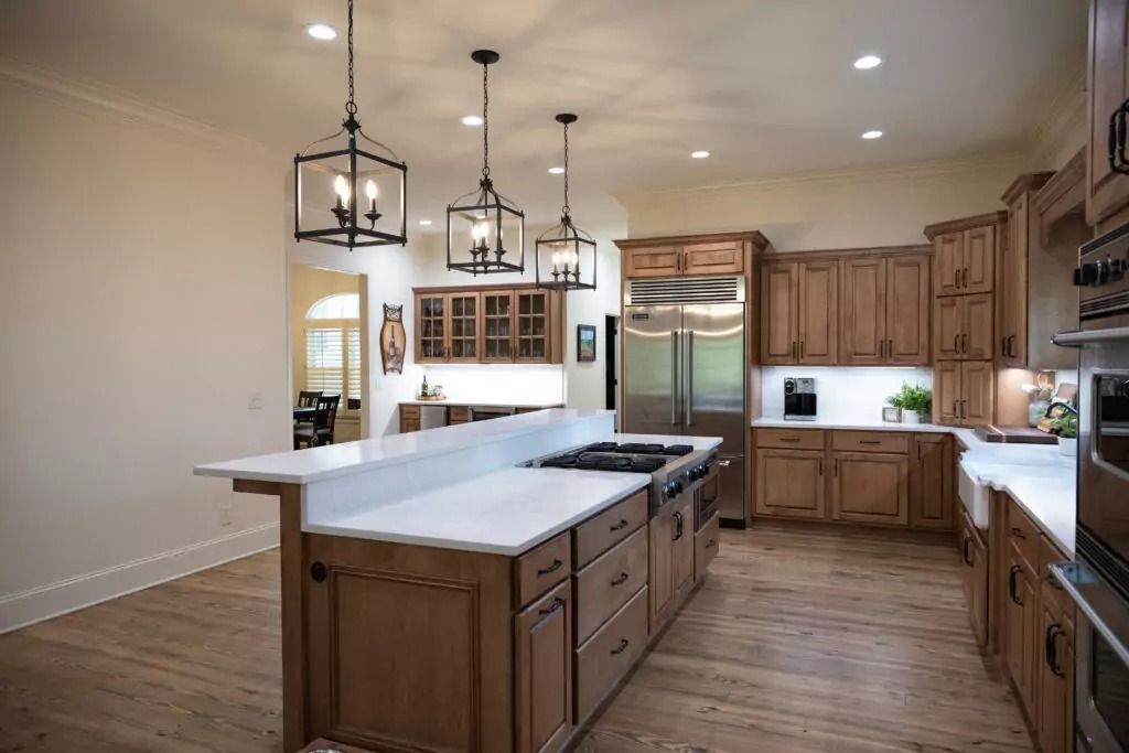 A kitchen with wooden cabinets , white counter tops , stainless steel appliances and a large island.