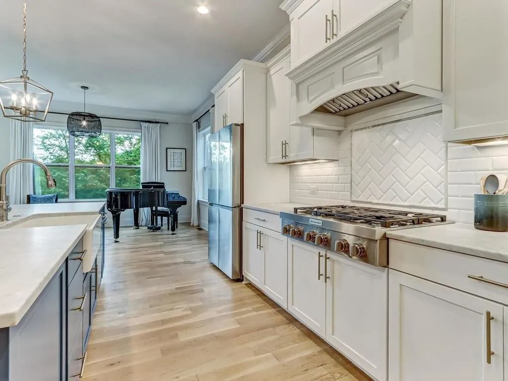 A kitchen with white cabinets and stainless steel appliances and a piano in the background.