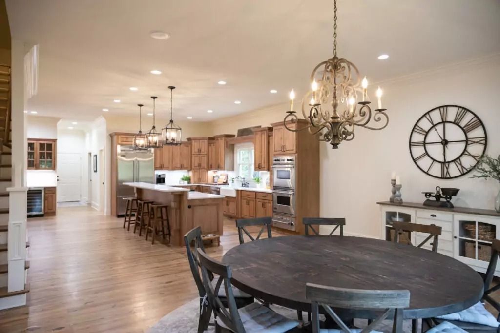 A dining room table and chairs in a kitchen with a large clock on the wall.