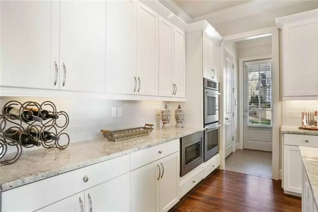 A kitchen with white cabinets , granite counter tops , stainless steel appliances and a wine rack.