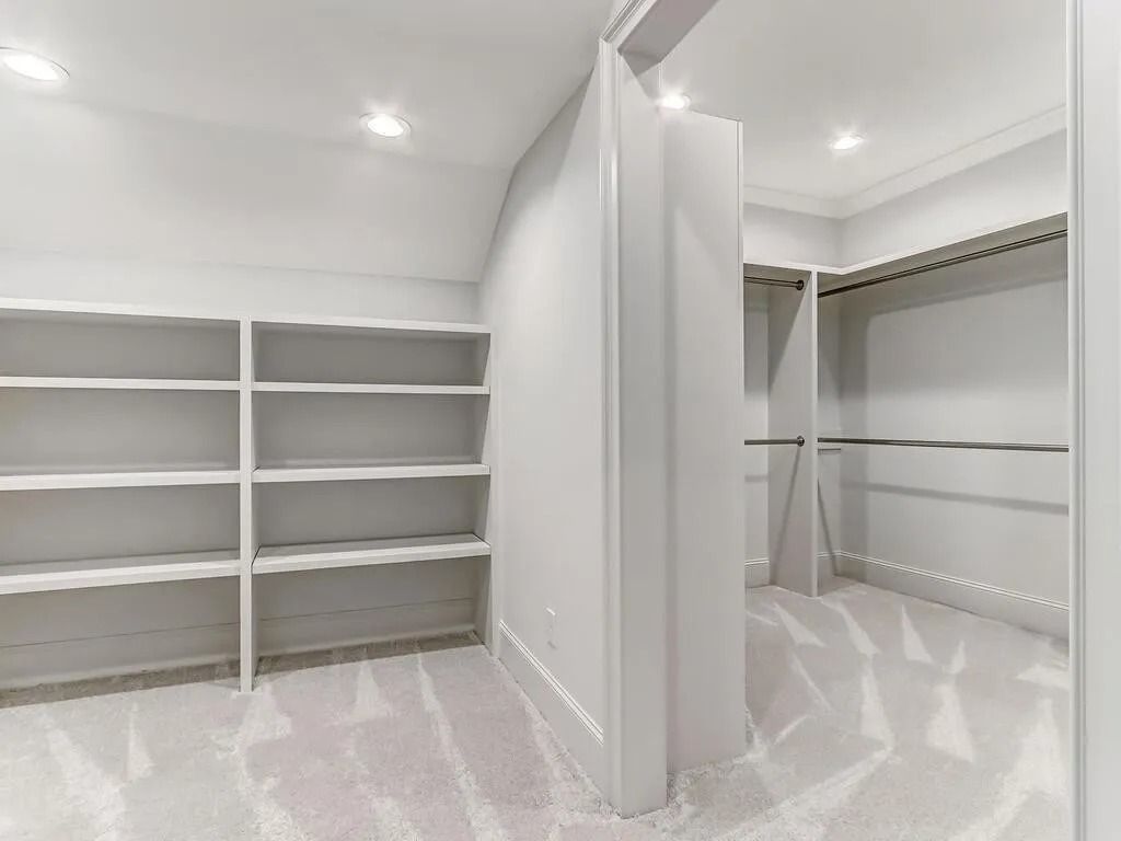 A walk in closet with white shelves and a carpeted floor.