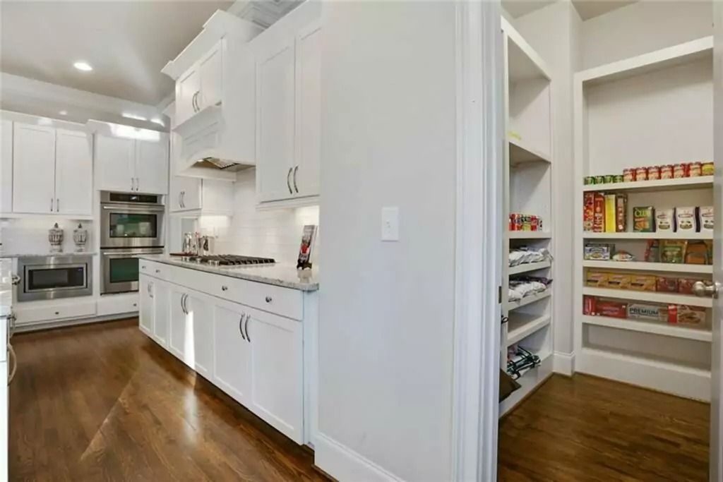 A kitchen with white cabinets and hardwood floors and a pantry.