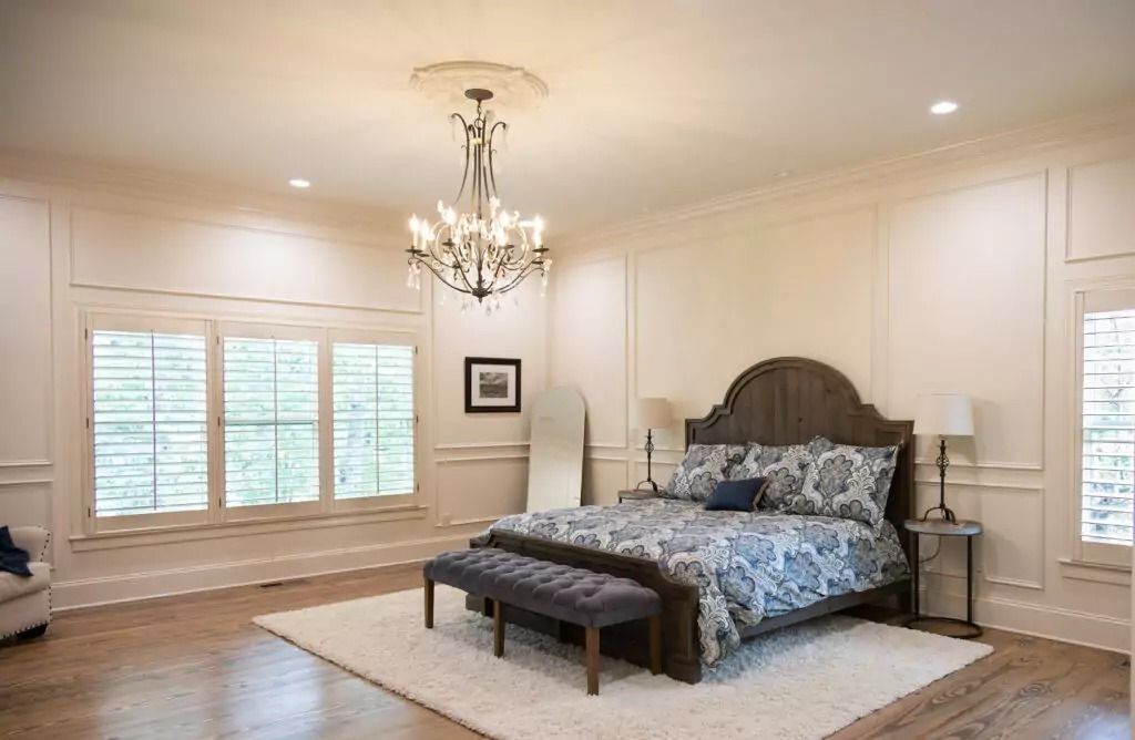 A bedroom with a large bed , a bench , a chandelier and lots of windows.