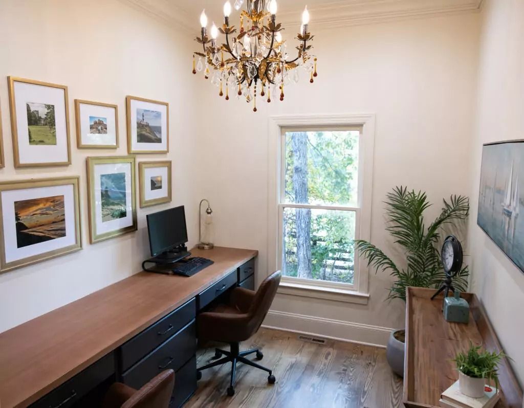 A home office with a desk , chair , computer and chandelier.