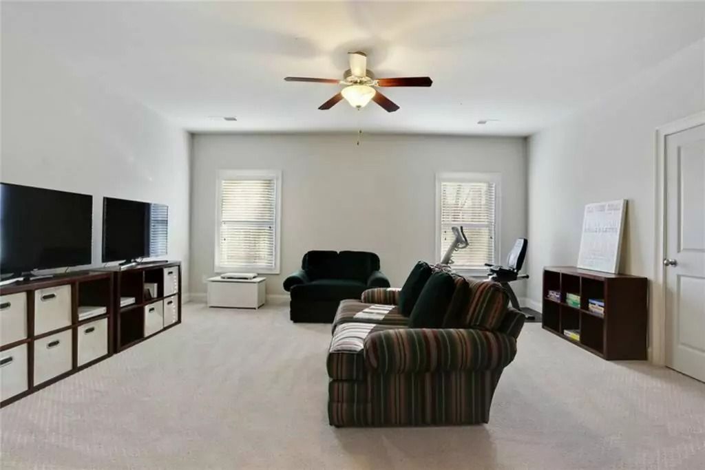 A living room with a couch , chair , televisions and a ceiling fan.