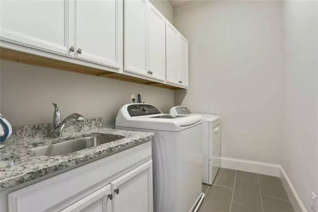 A laundry room with a sink , washer and dryer , and granite counter tops.