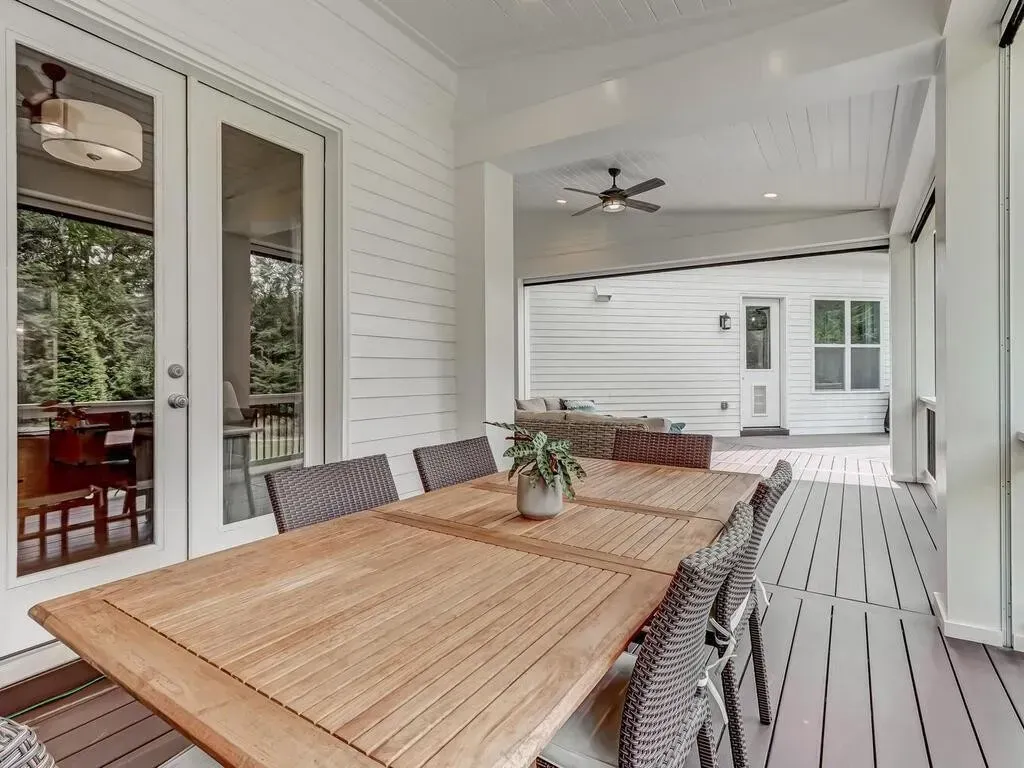 A patio with a wooden table and chairs and a ceiling fan.