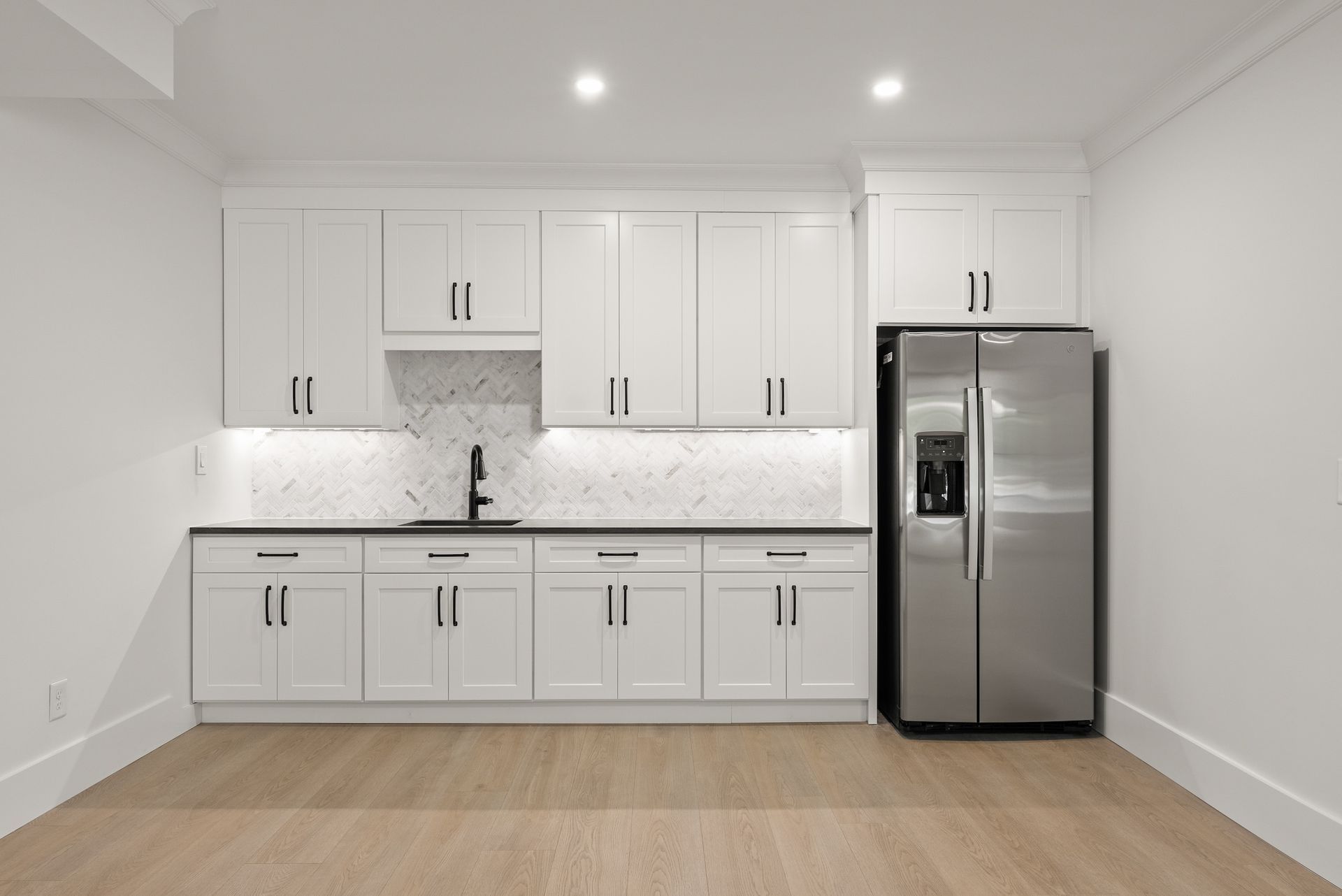 An empty kitchen with white cabinets and a stainless steel refrigerator.
