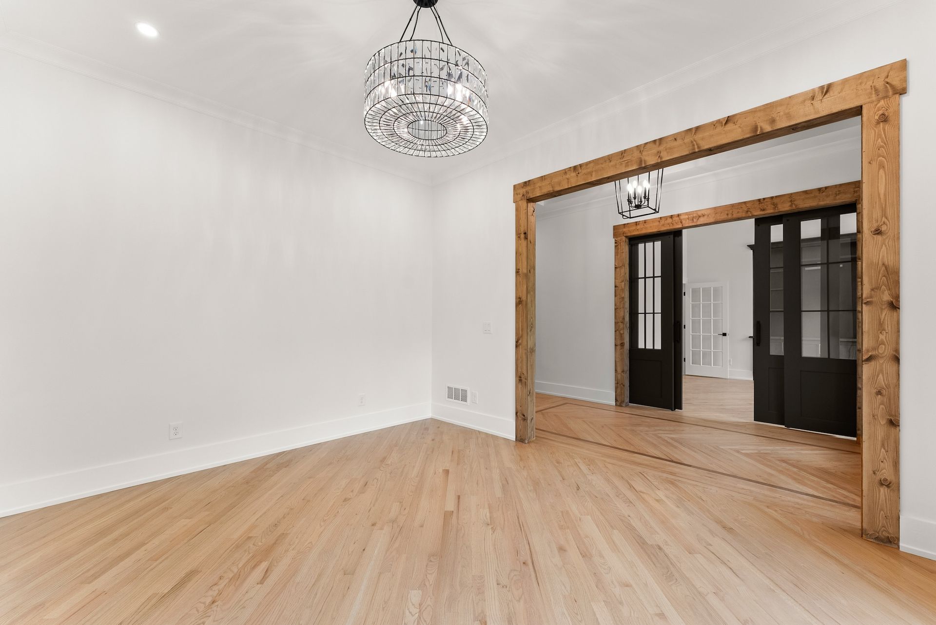 An empty room with hardwood floors and a chandelier hanging from the ceiling.