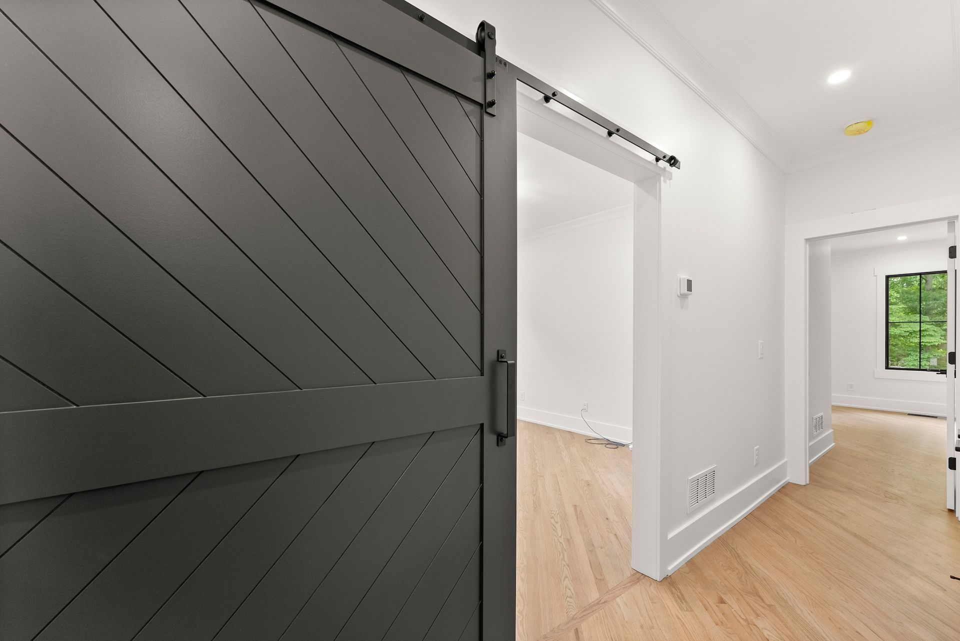 A black sliding barn door is open to a hallway in a house.