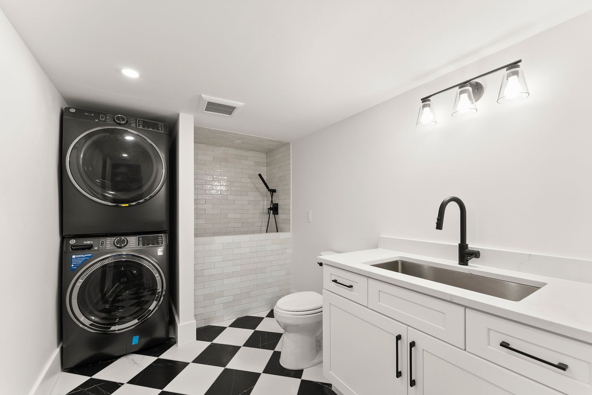 A bathroom with a washer and dryer stacked on top of each other and a sink.