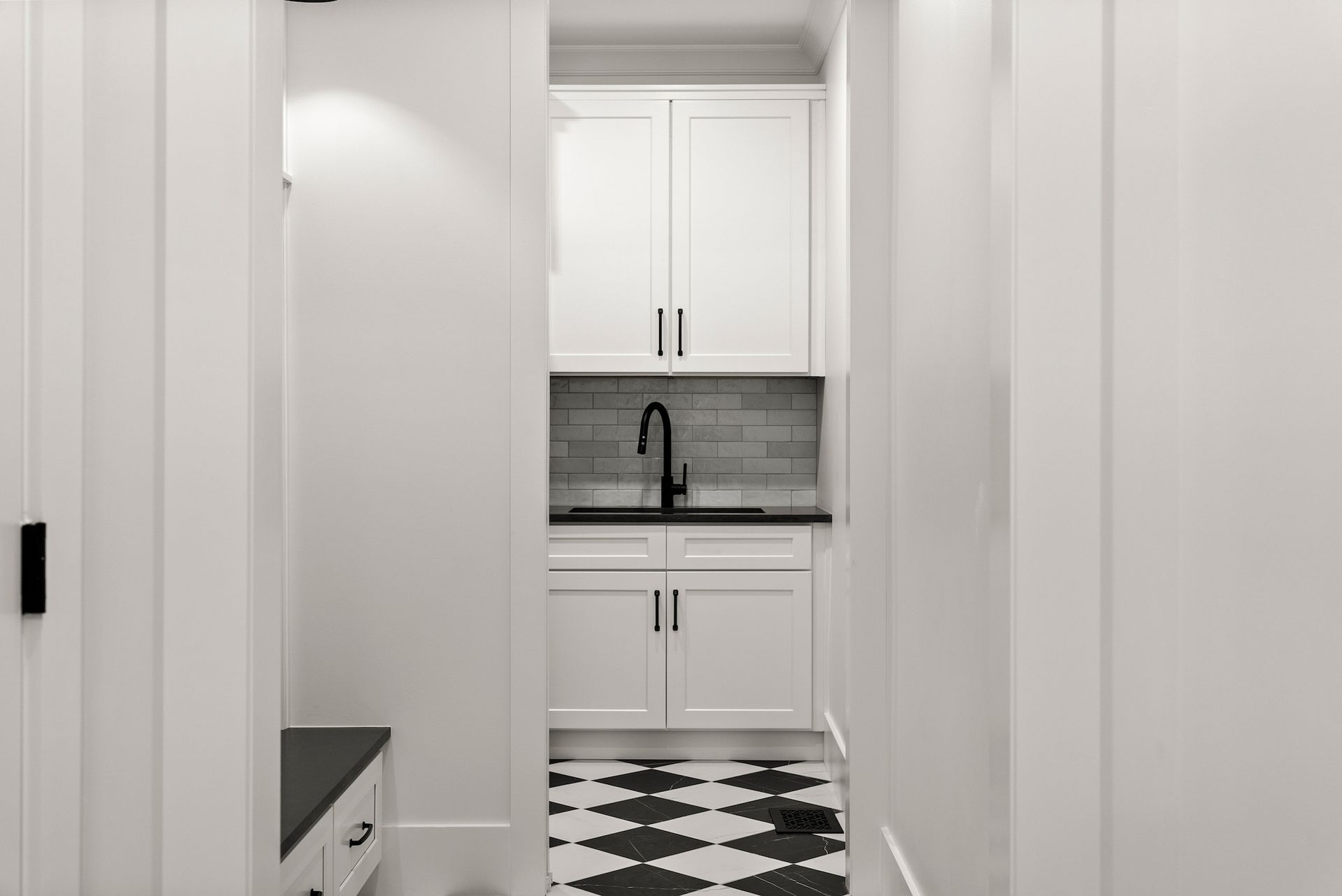 A laundry room with white cabinets and a black and white checkered floor.