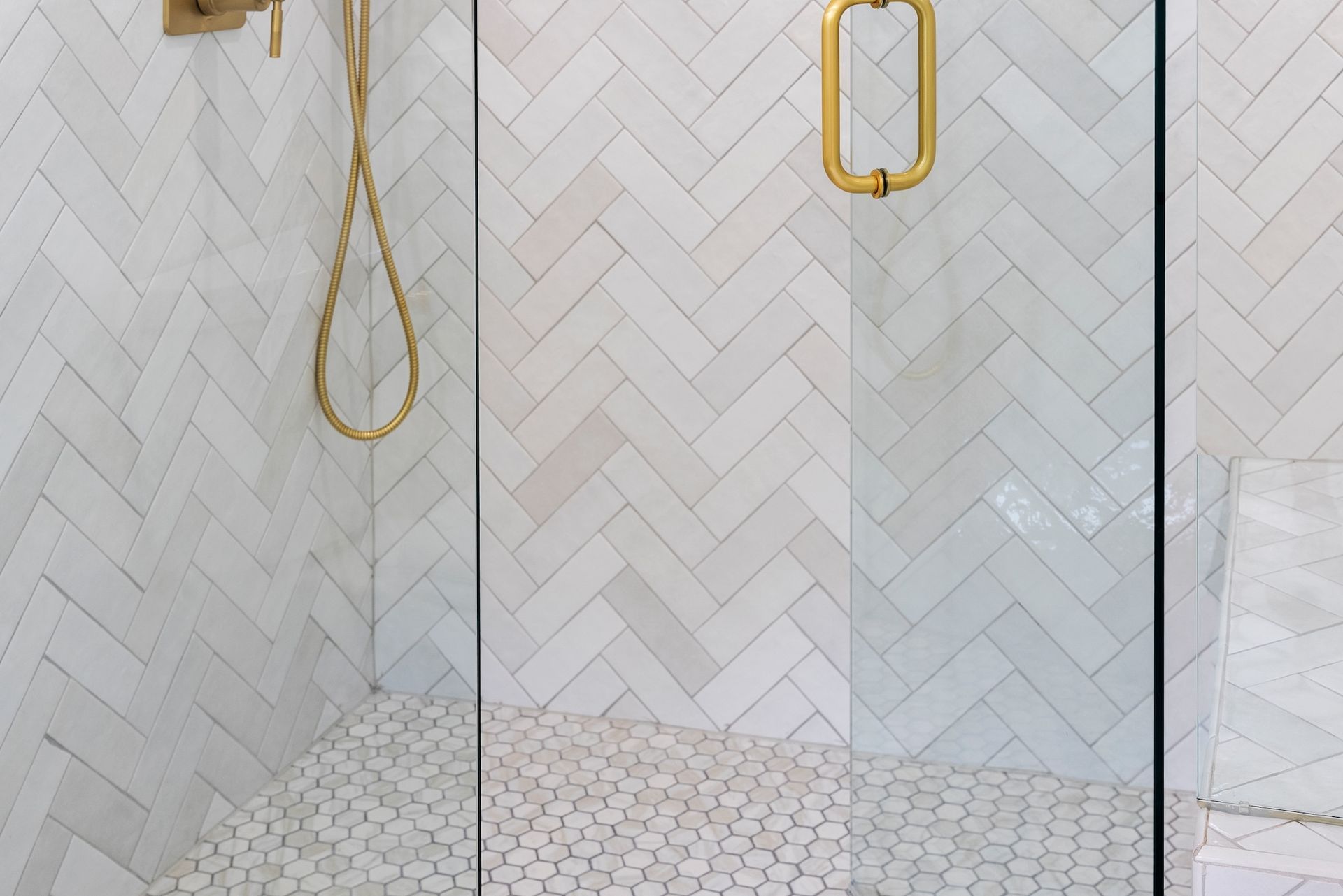 A bathroom with white tiles and a walk in shower with a glass door.