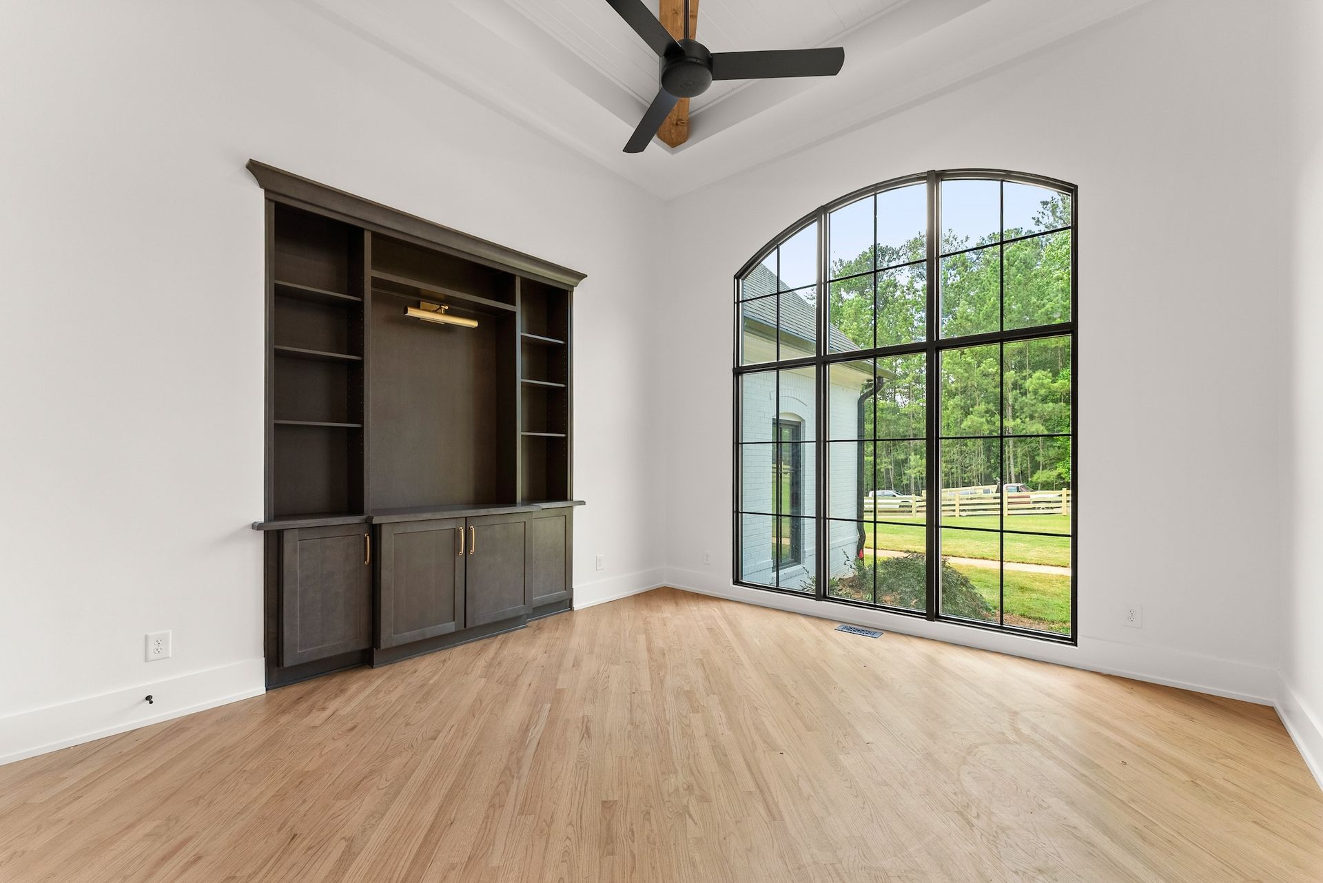 An empty living room with a large window and a ceiling fan.