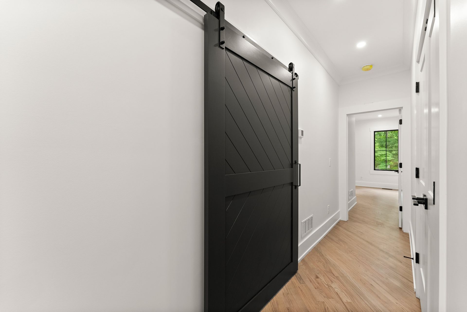A black sliding barn door is hanging on a white wall in a hallway.
