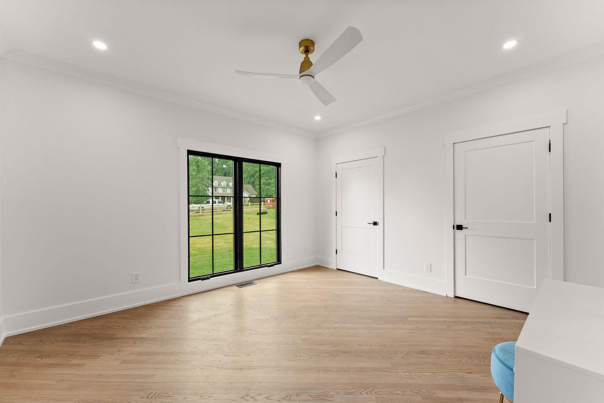 An empty room with a ceiling fan and two windows.