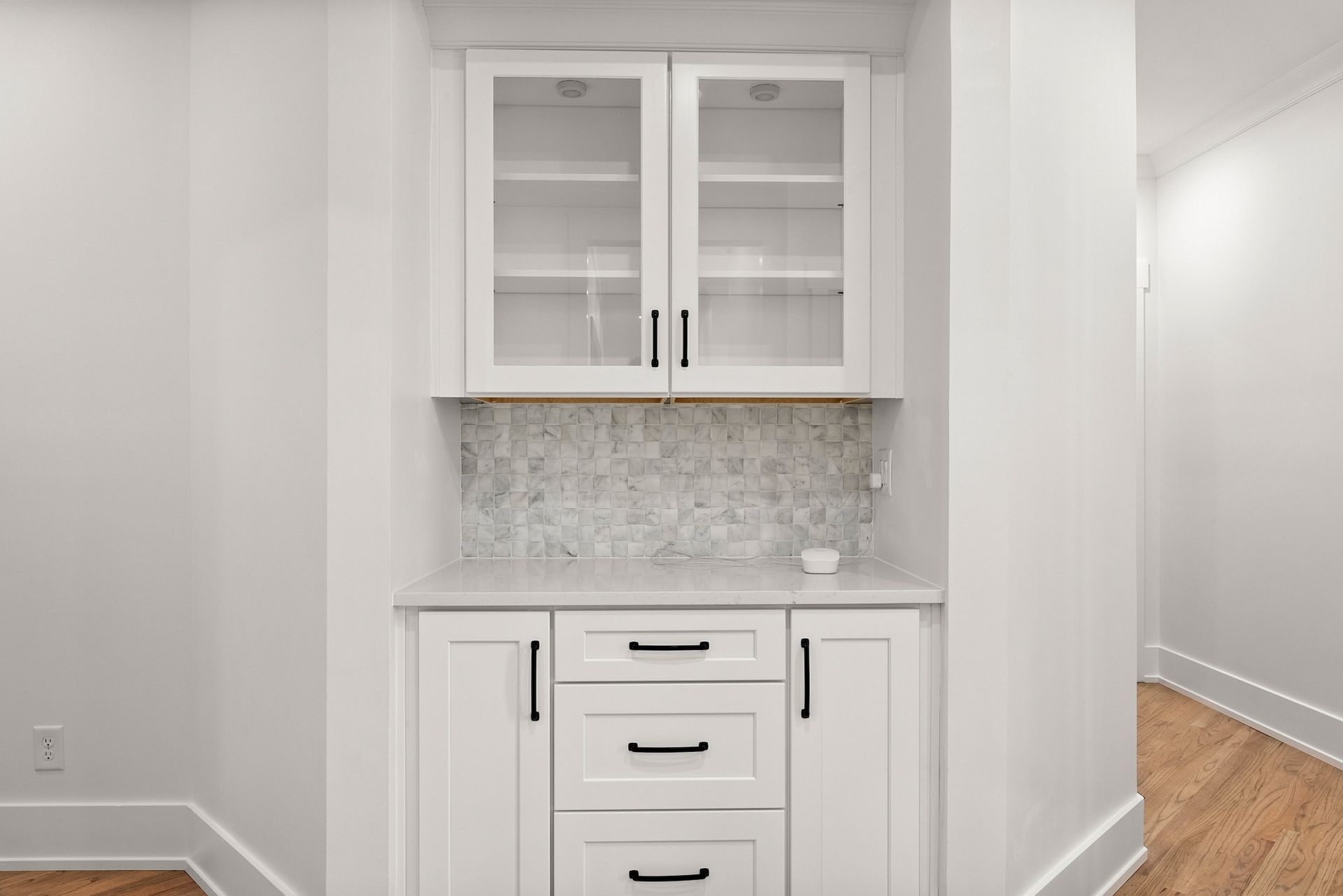 A kitchen with white cabinets , drawers , and glass doors.