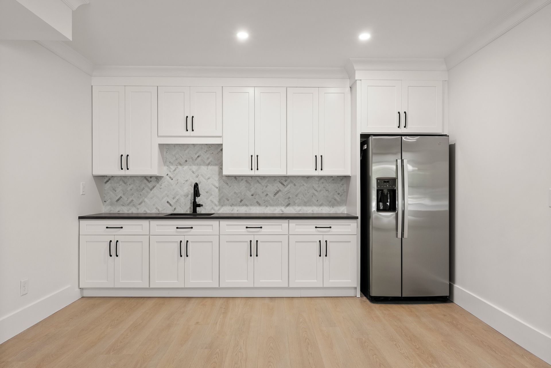 An empty kitchen with white cabinets and a stainless steel refrigerator
