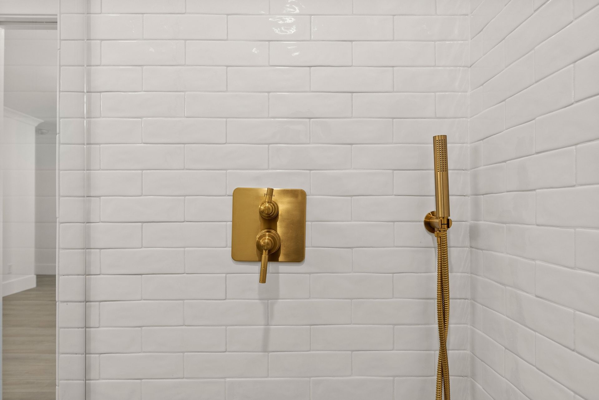 A bathroom with white tiles and a gold shower head.