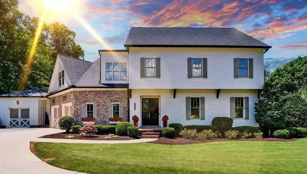 A large white house with a lot of windows is sitting on top of a lush green lawn.