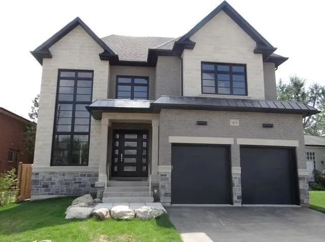 Two-story house with light gray stucco, stone accents, black windows and garage doors.