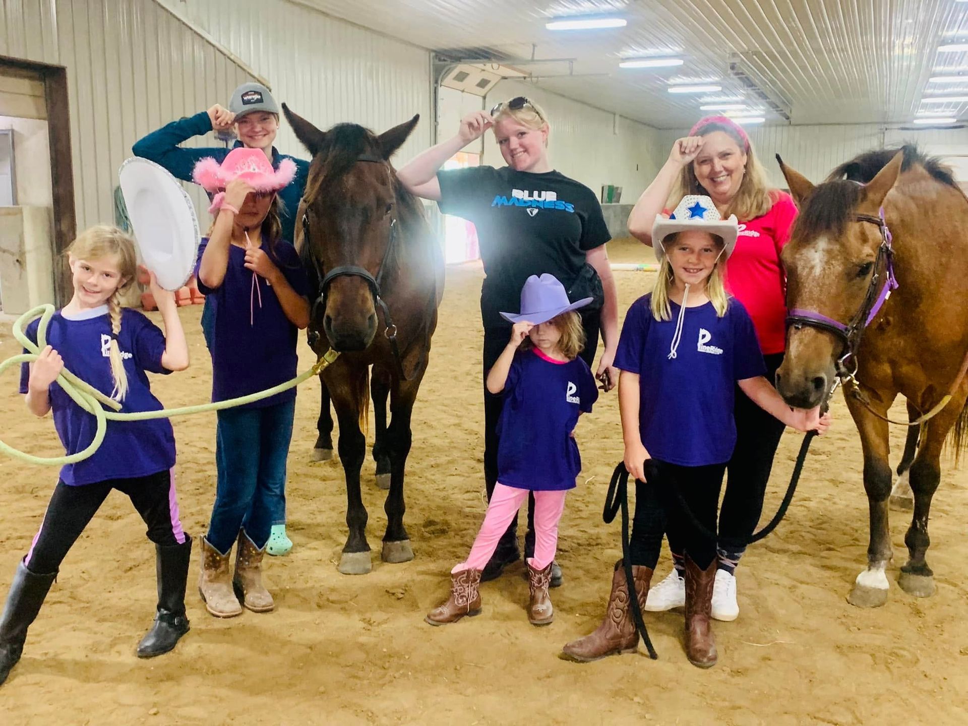 A group of people standing next to horses in a barn.