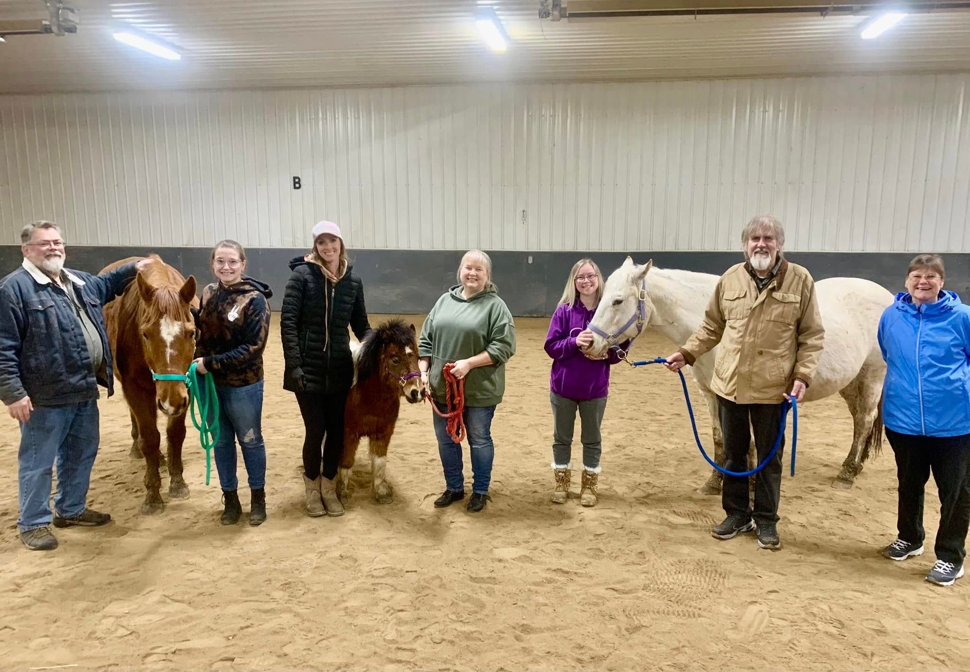 A group of people standing next to horses in a barn.