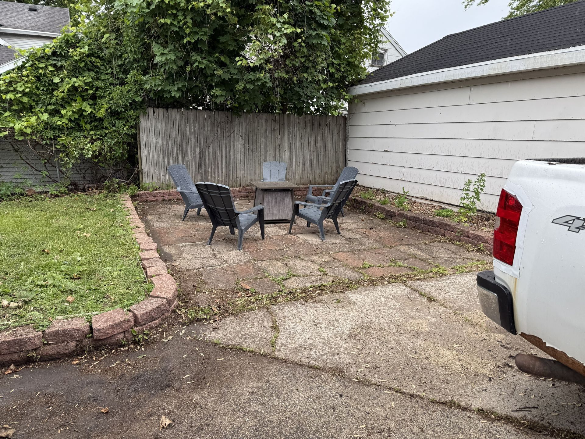 Backyard patio with chairs, small table, wooden fence, and concrete driveway.