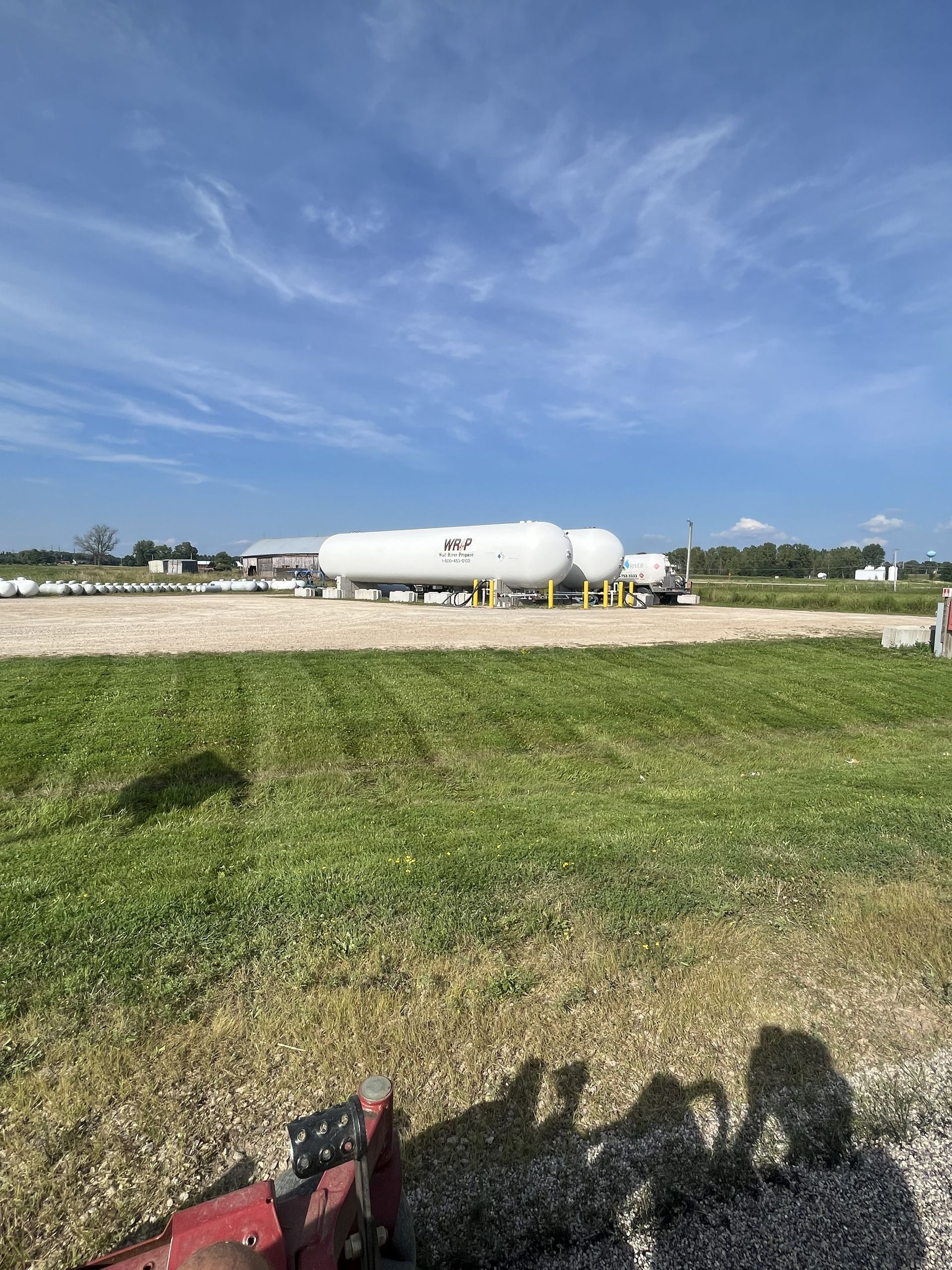 White propane tanks in a field under a blue sky with some clouds.