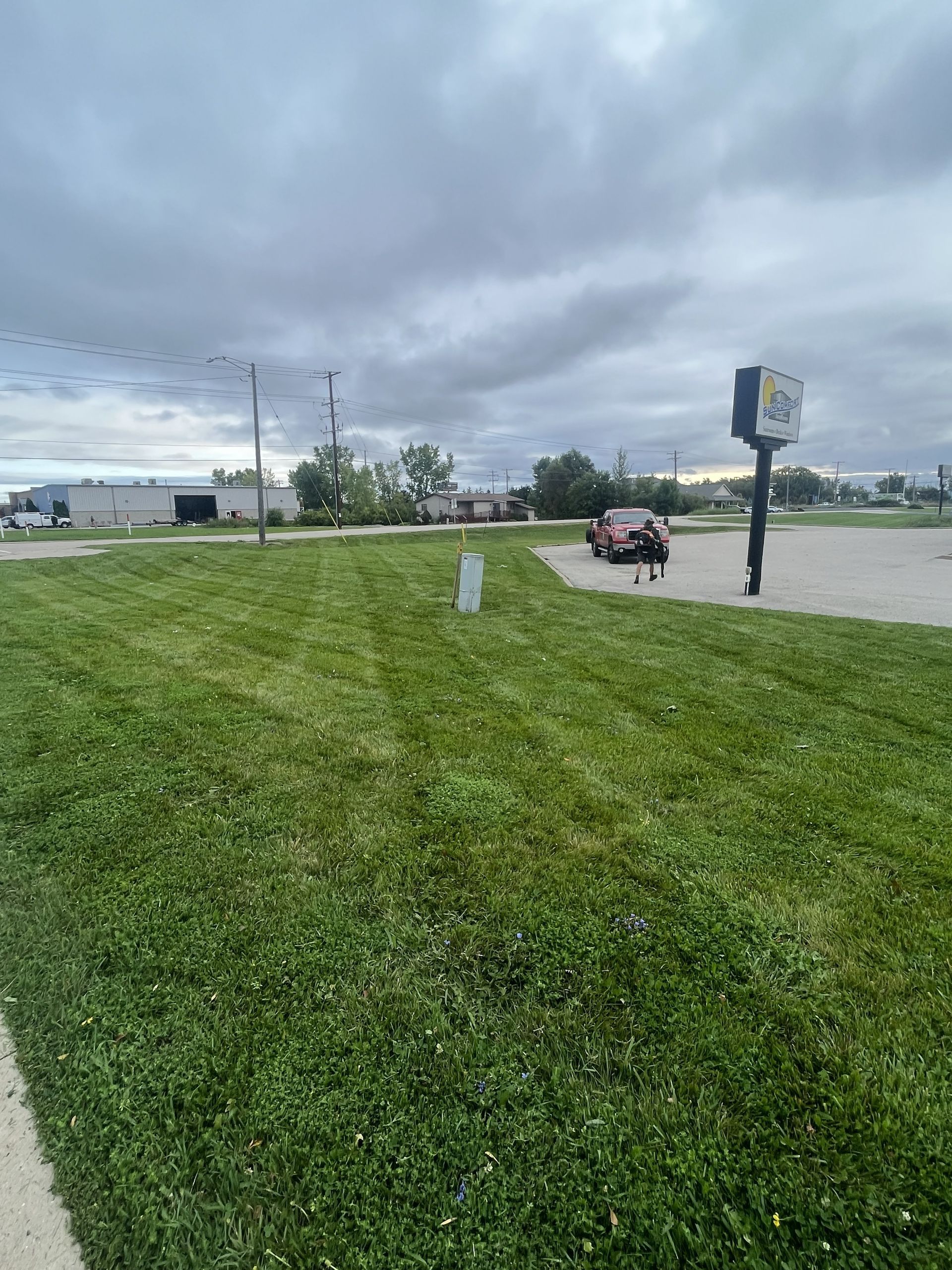 Lawn with a car and sign under a cloudy sky.