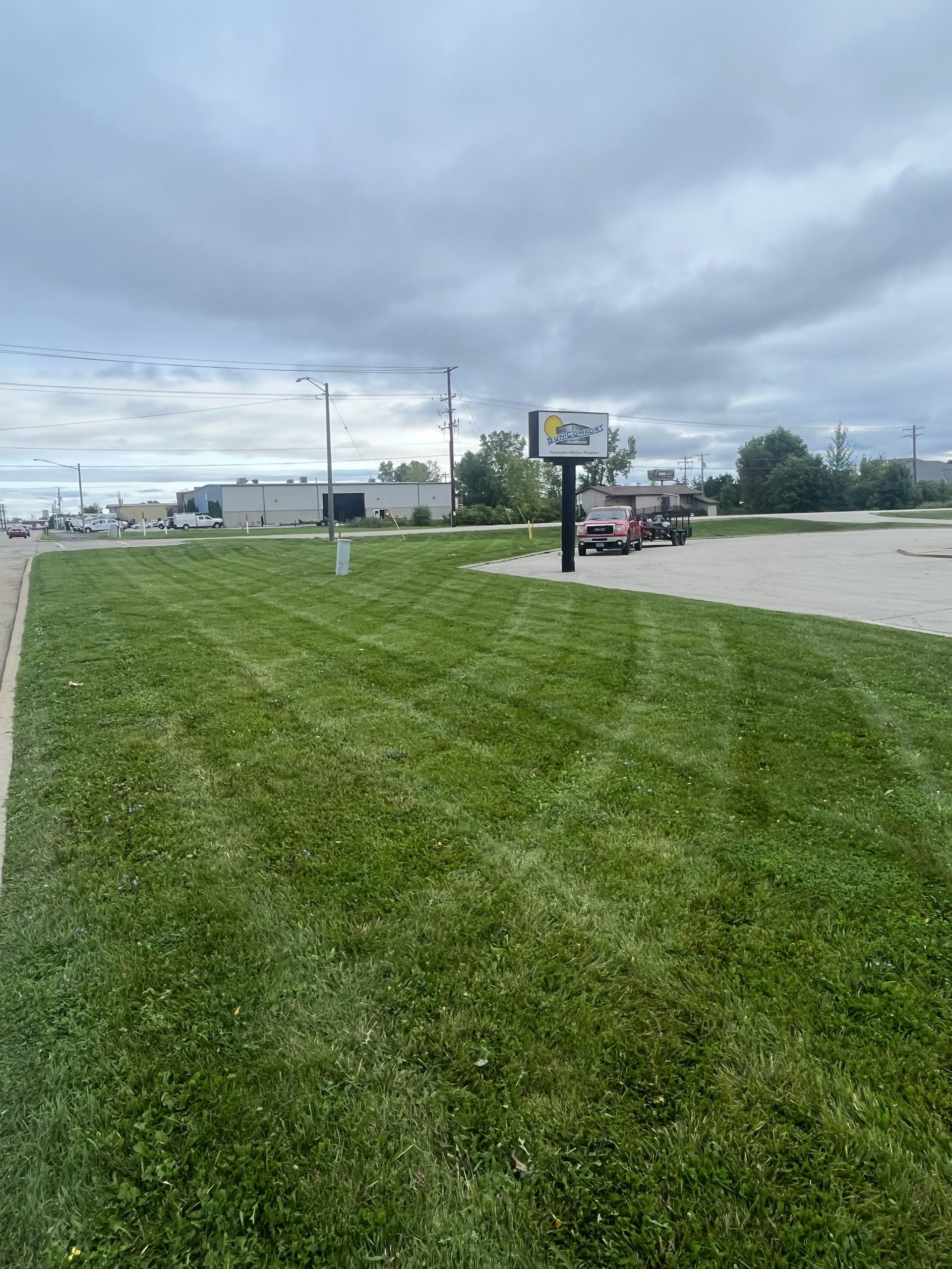 Lush green lawn with freshly cut lines, roadside sign, cloudy sky, parking lot in the distance.