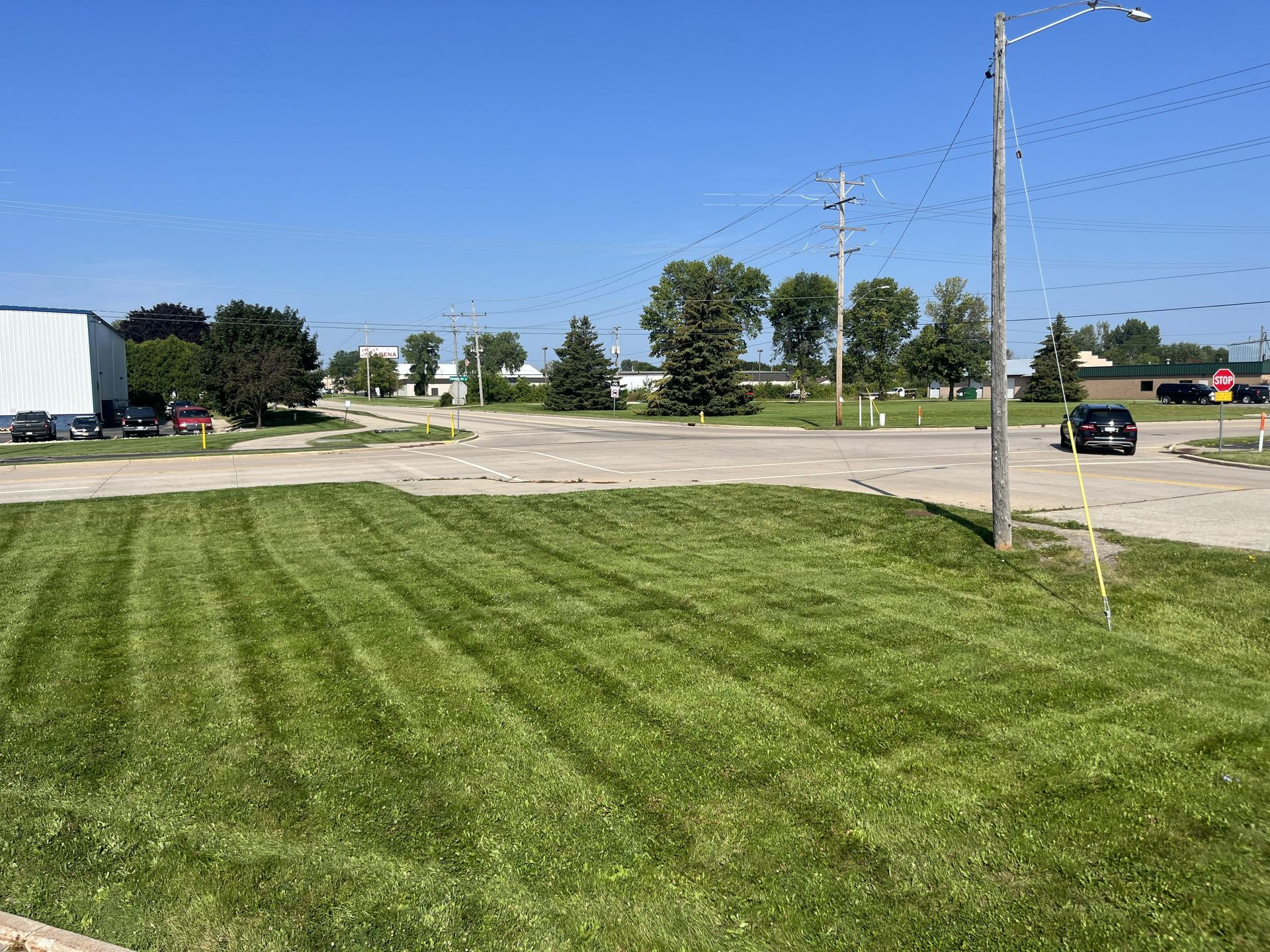 Well-mowed green lawn in foreground, road with car, power lines, and blue sky.