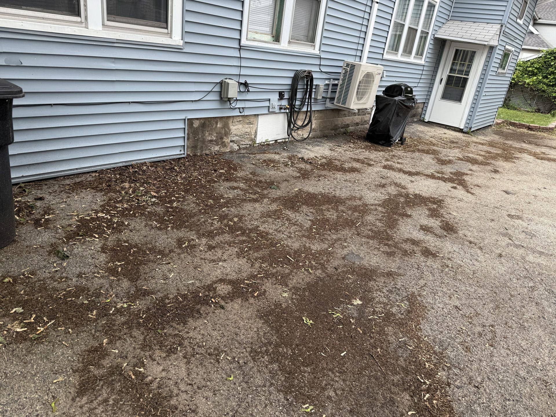 Side of a light blue house with gravel yard; trash can, and debris. White door.