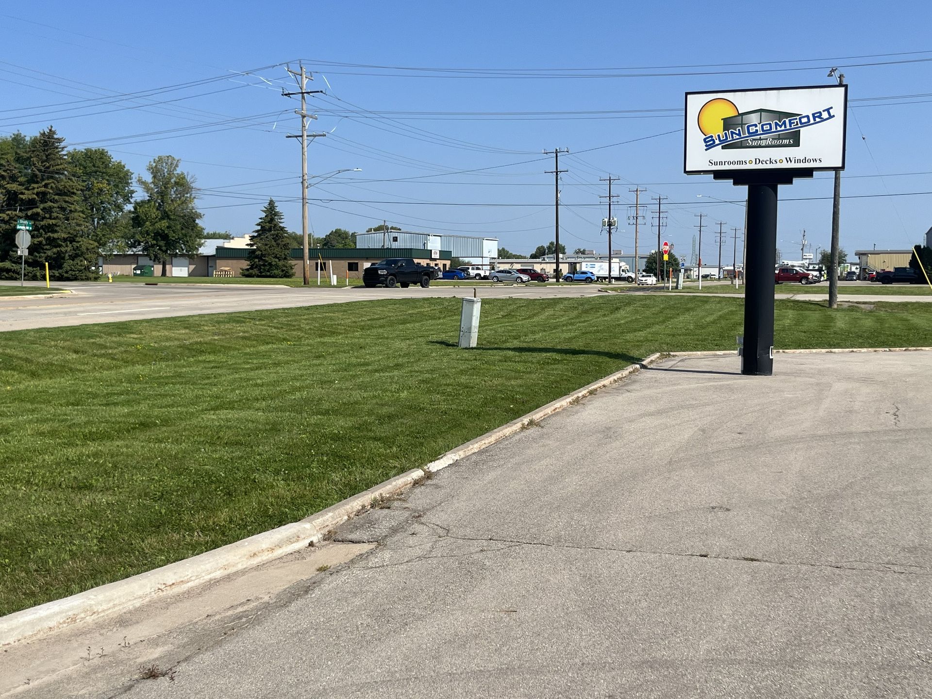 Grassy area in front of a sign for a business; sunny, clear day with power lines and some cars in the distance.