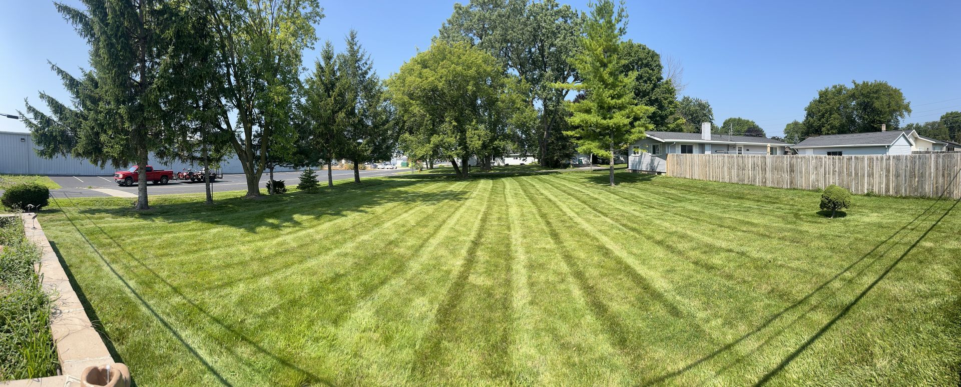 Green lawn with freshly cut stripes, trees, fence, and a clear blue sky.