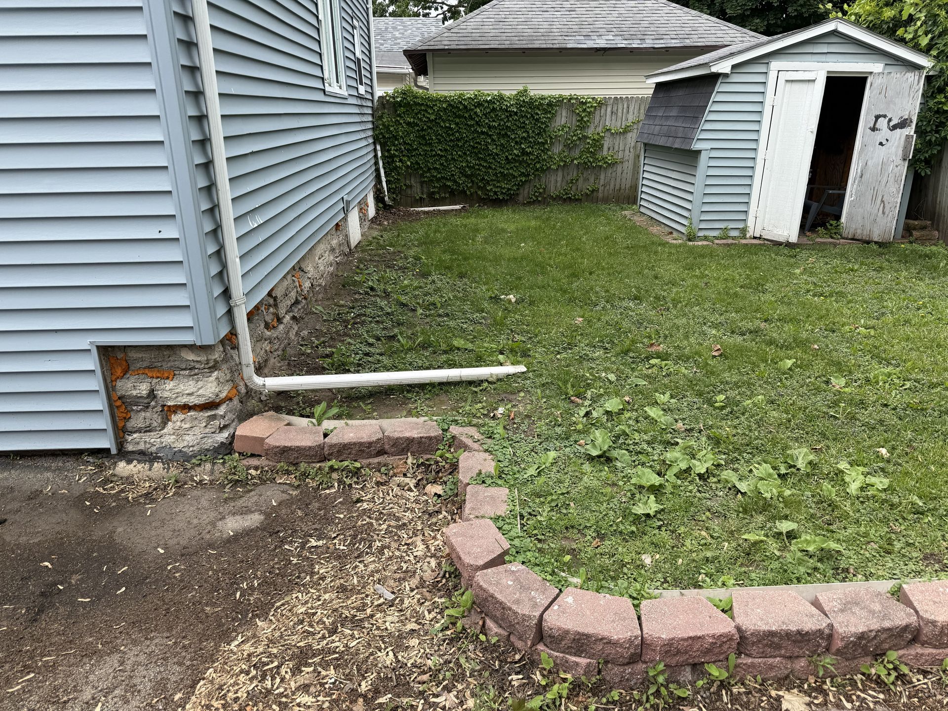 Side of a light blue house, grass, and a small shed in a backyard setting.