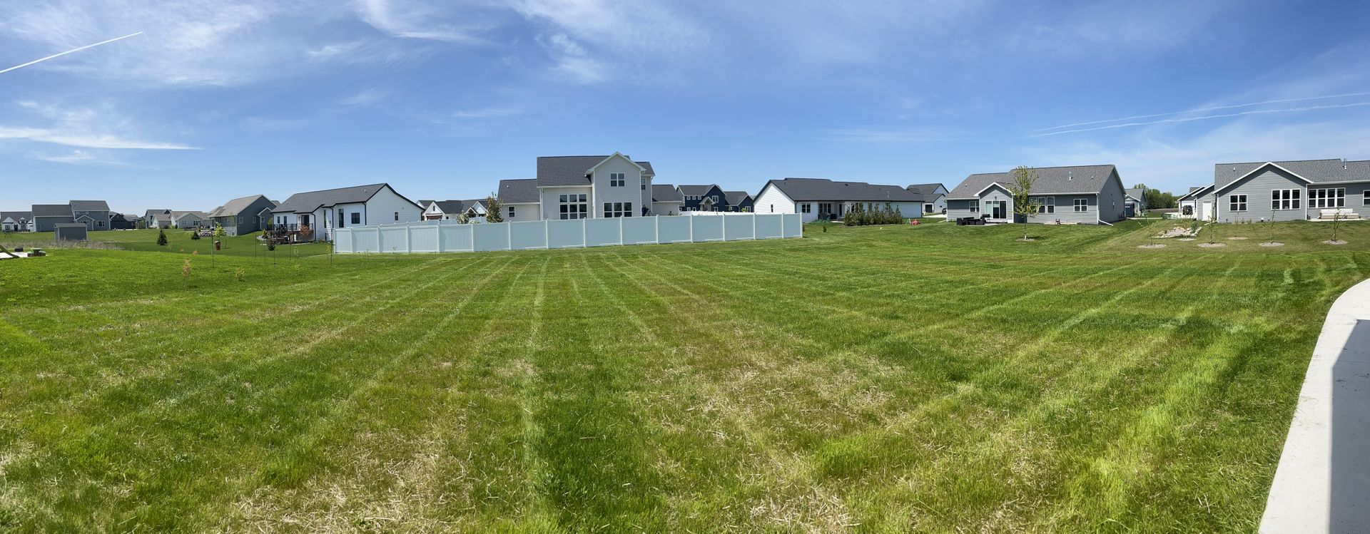 A wide, grassy field with houses in the background on a sunny day.