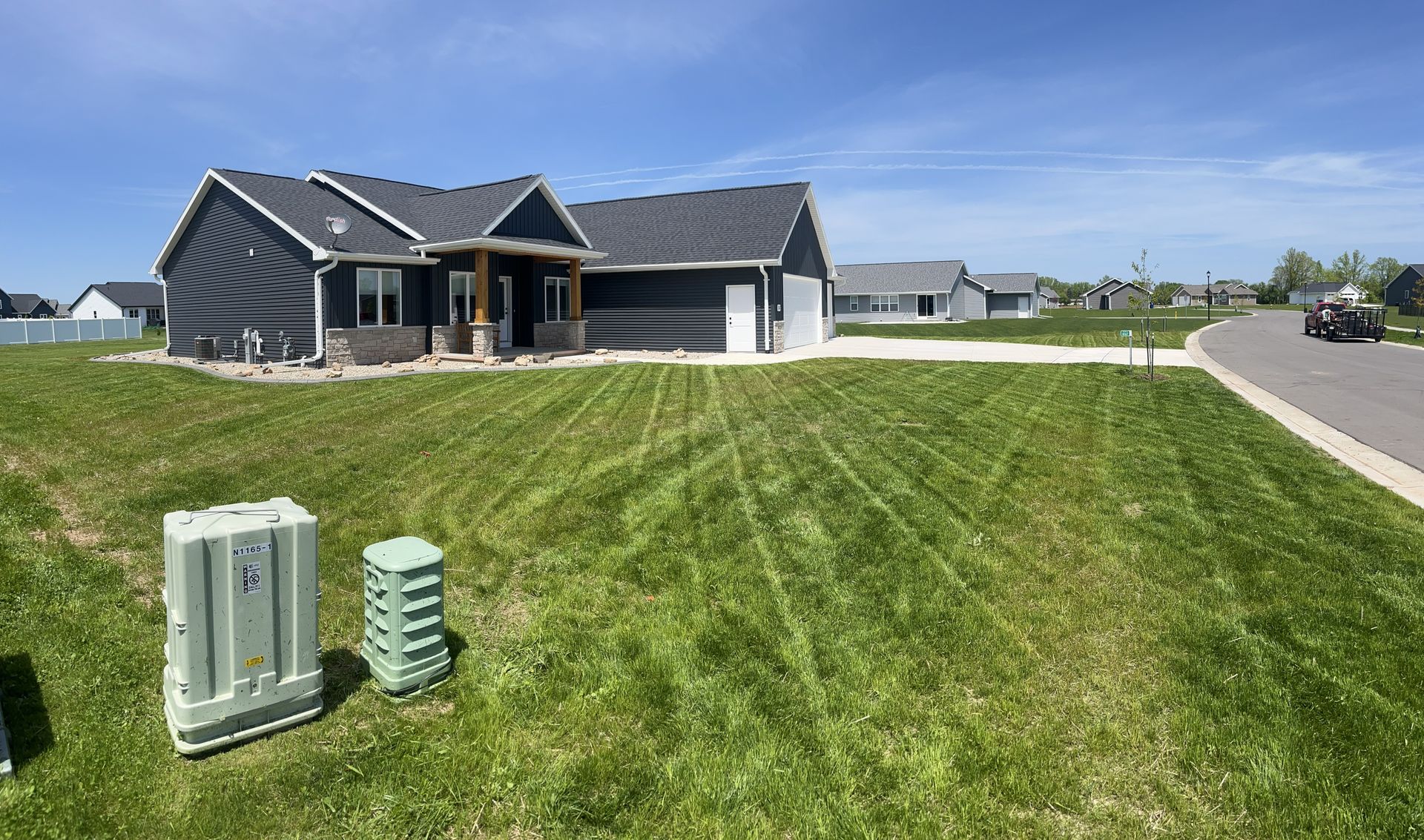 Gray house with a porch and attached garage on a grassy lot. Utility boxes in the front.