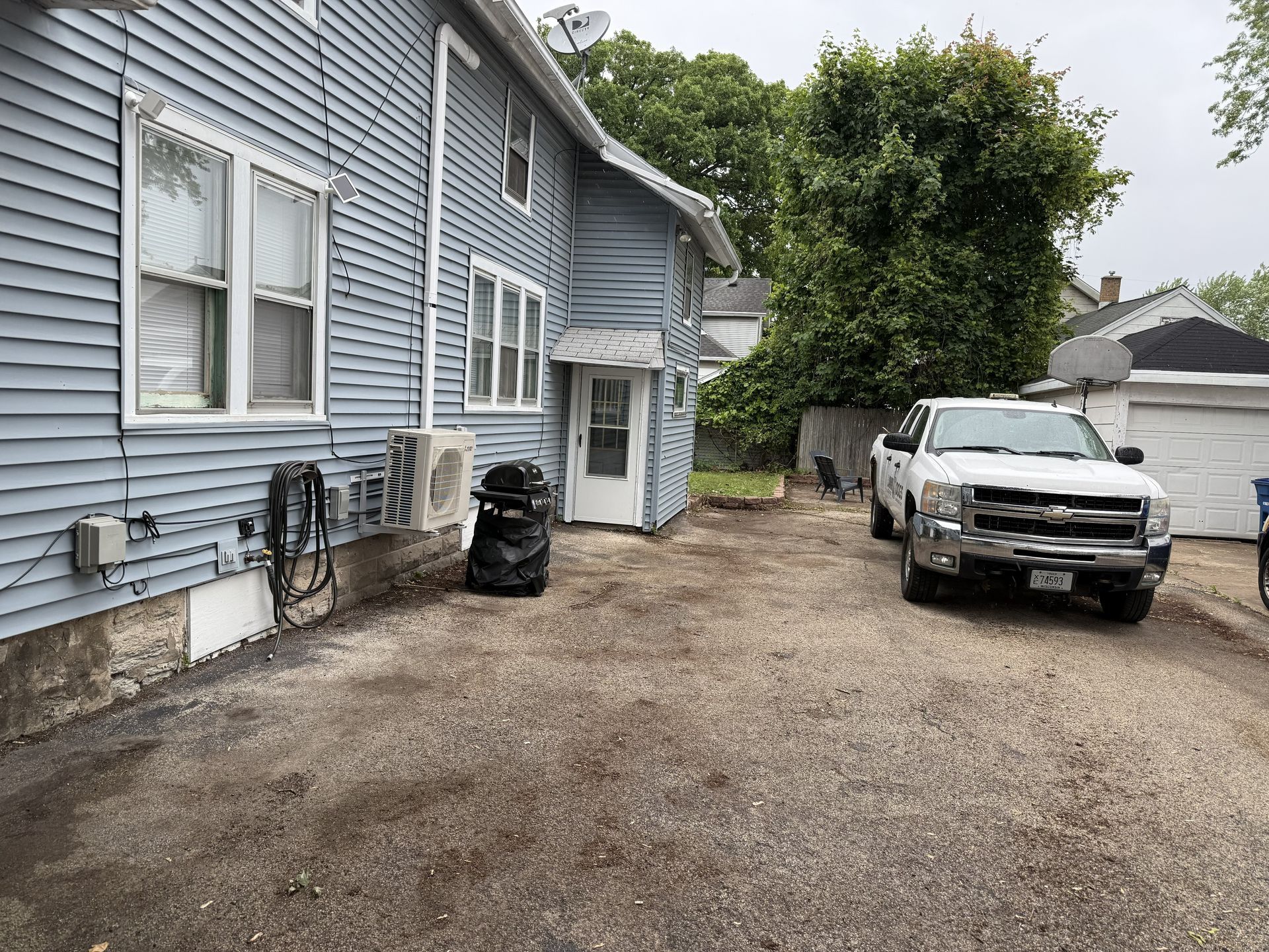 Side view of a blue house with white trim and a gravel driveway, white pickup truck parked.