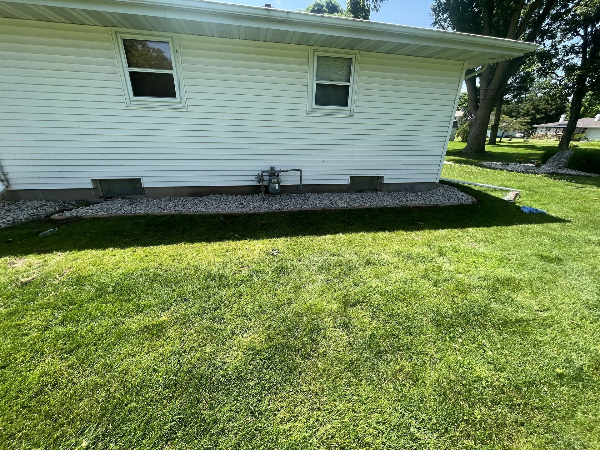 White house exterior with two windows and a gravel bed along the base, next to green grass.