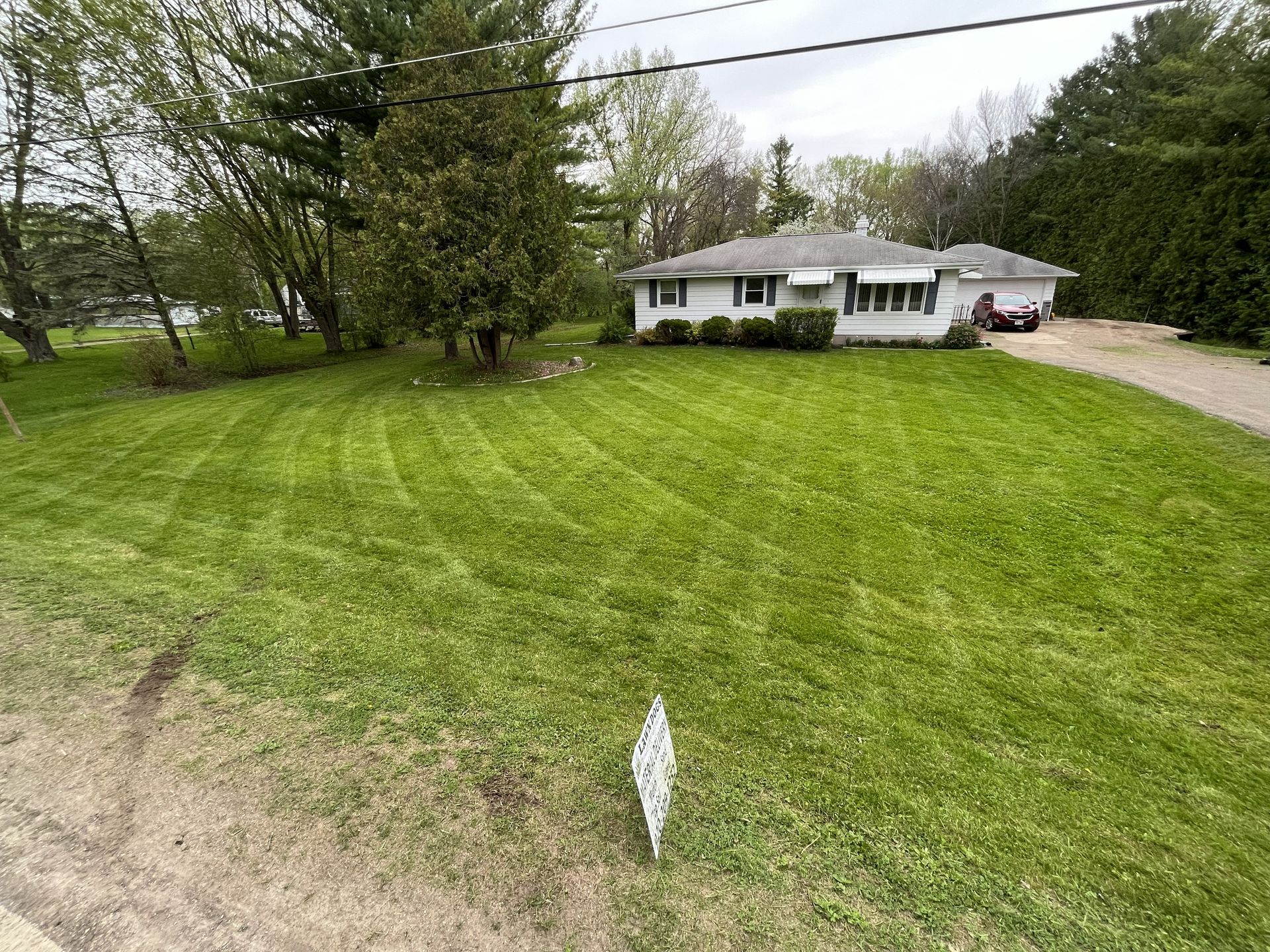 House with a white exterior, green lawn, trees, and driveway.