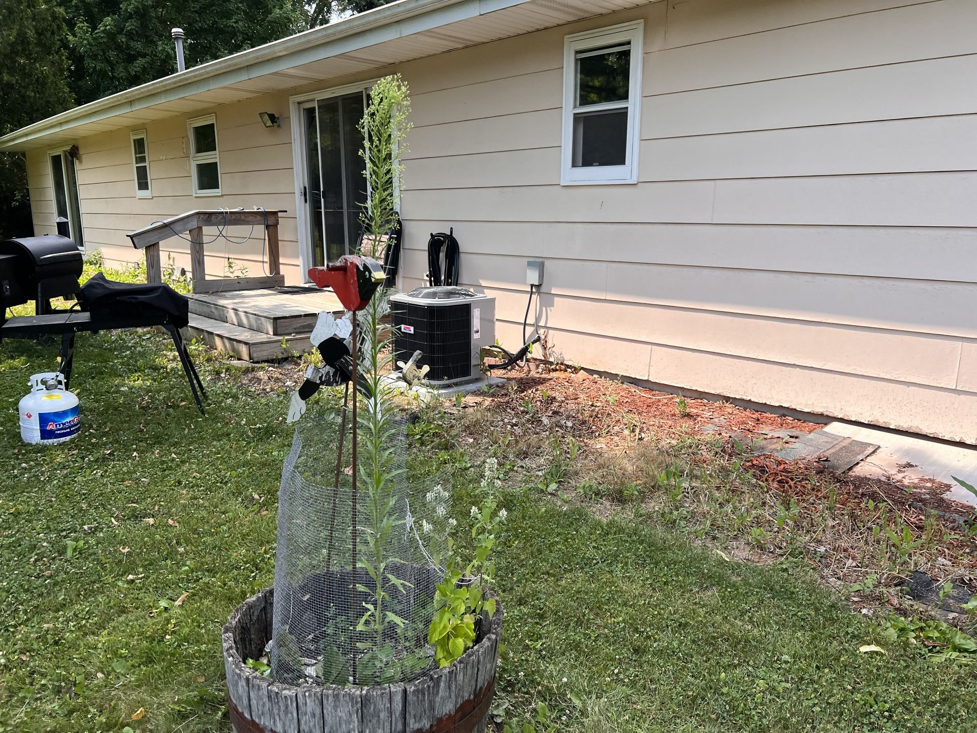 Backyard with a house, grill, potted plant, and air conditioning unit.