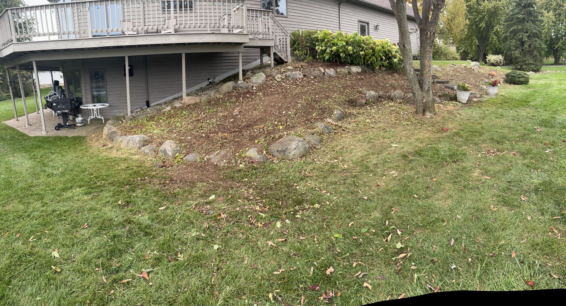 Backyard view with a deck, grassy area, and a rock-lined hill.