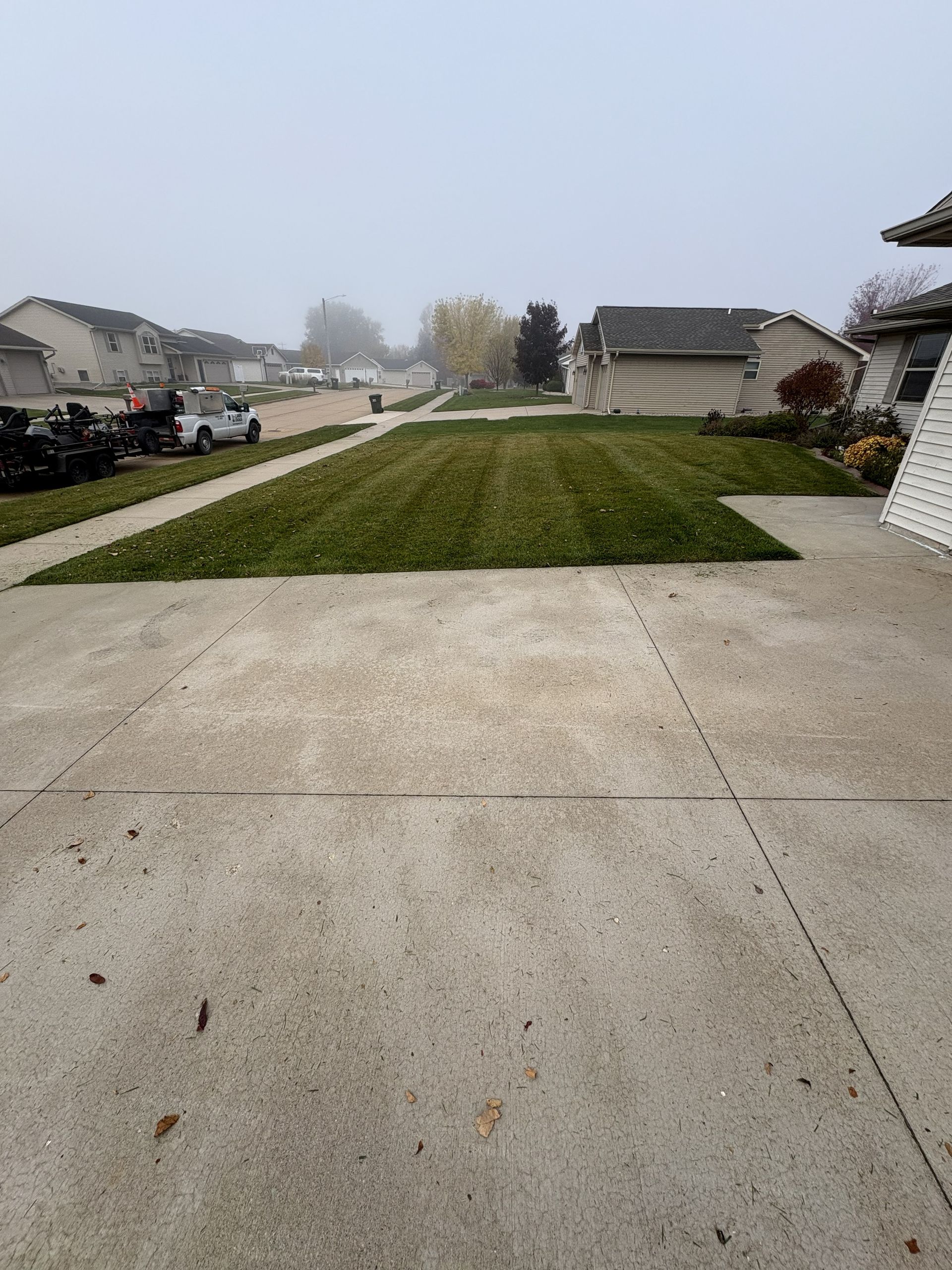 Concrete driveway with mowed lawn and street in foggy suburban neighborhood.