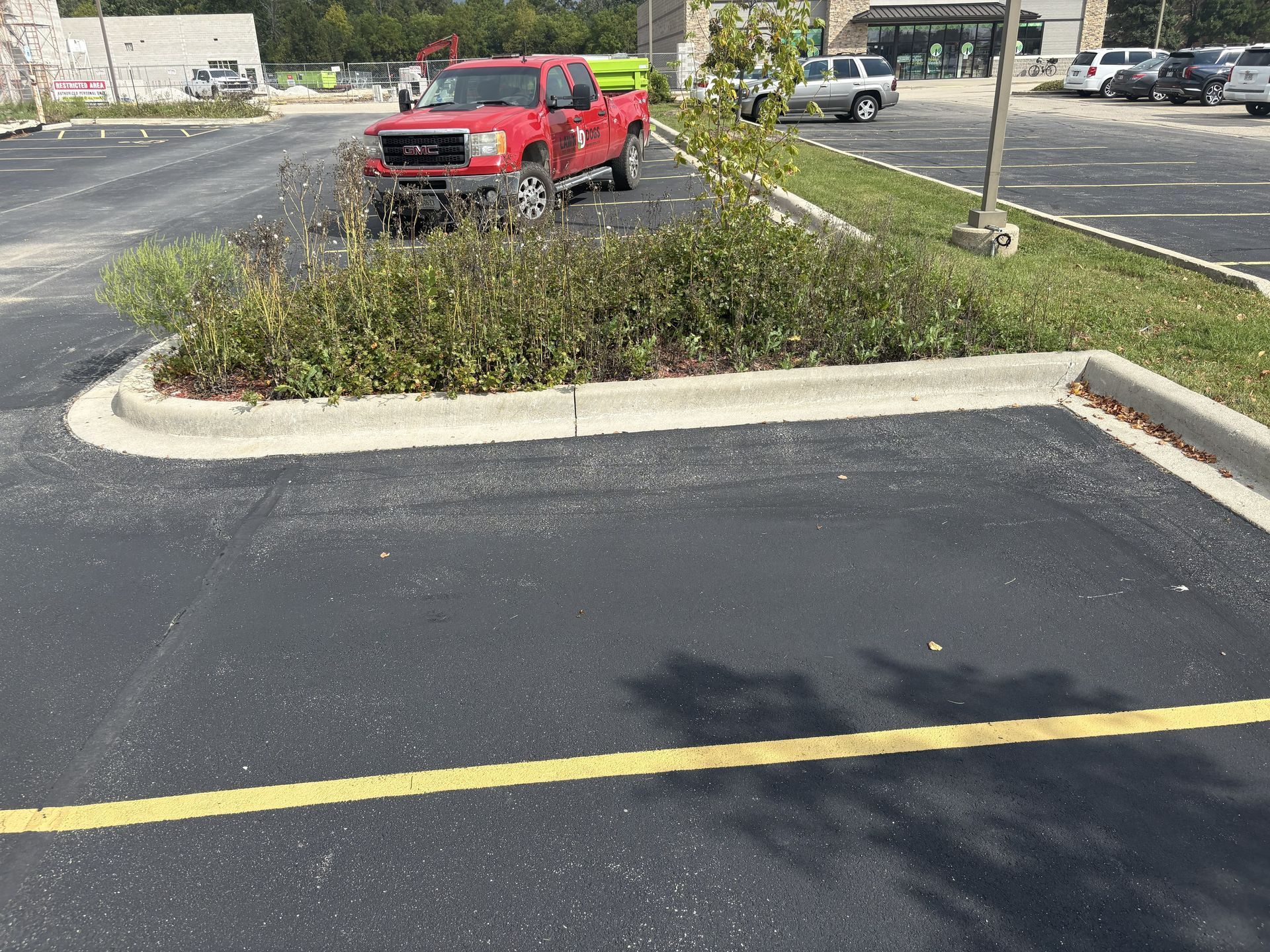 Red pickup truck parked next to a curb and landscaping in a parking lot.