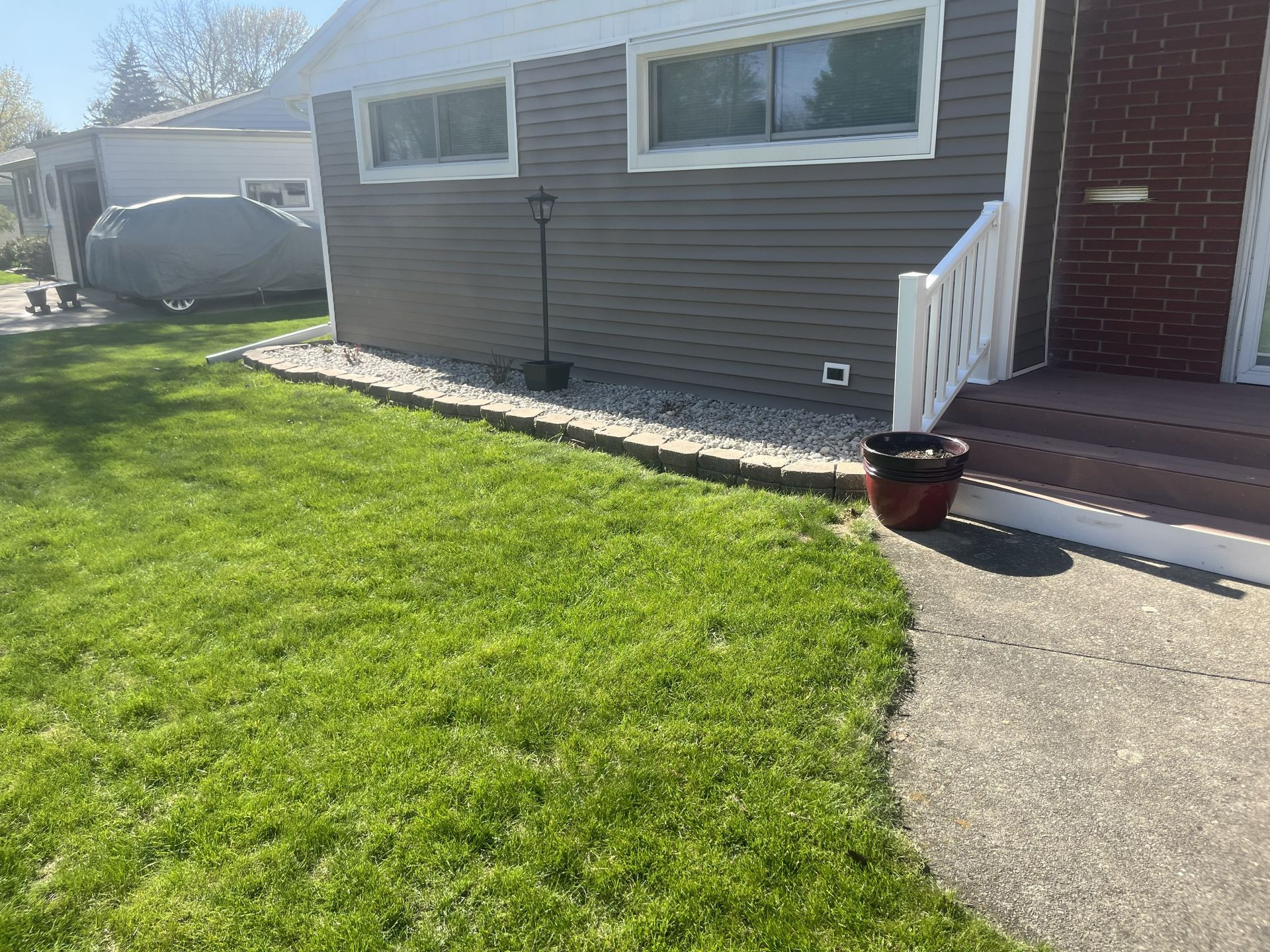 Green lawn bordered by stone, next to a gray house with a brick entry.