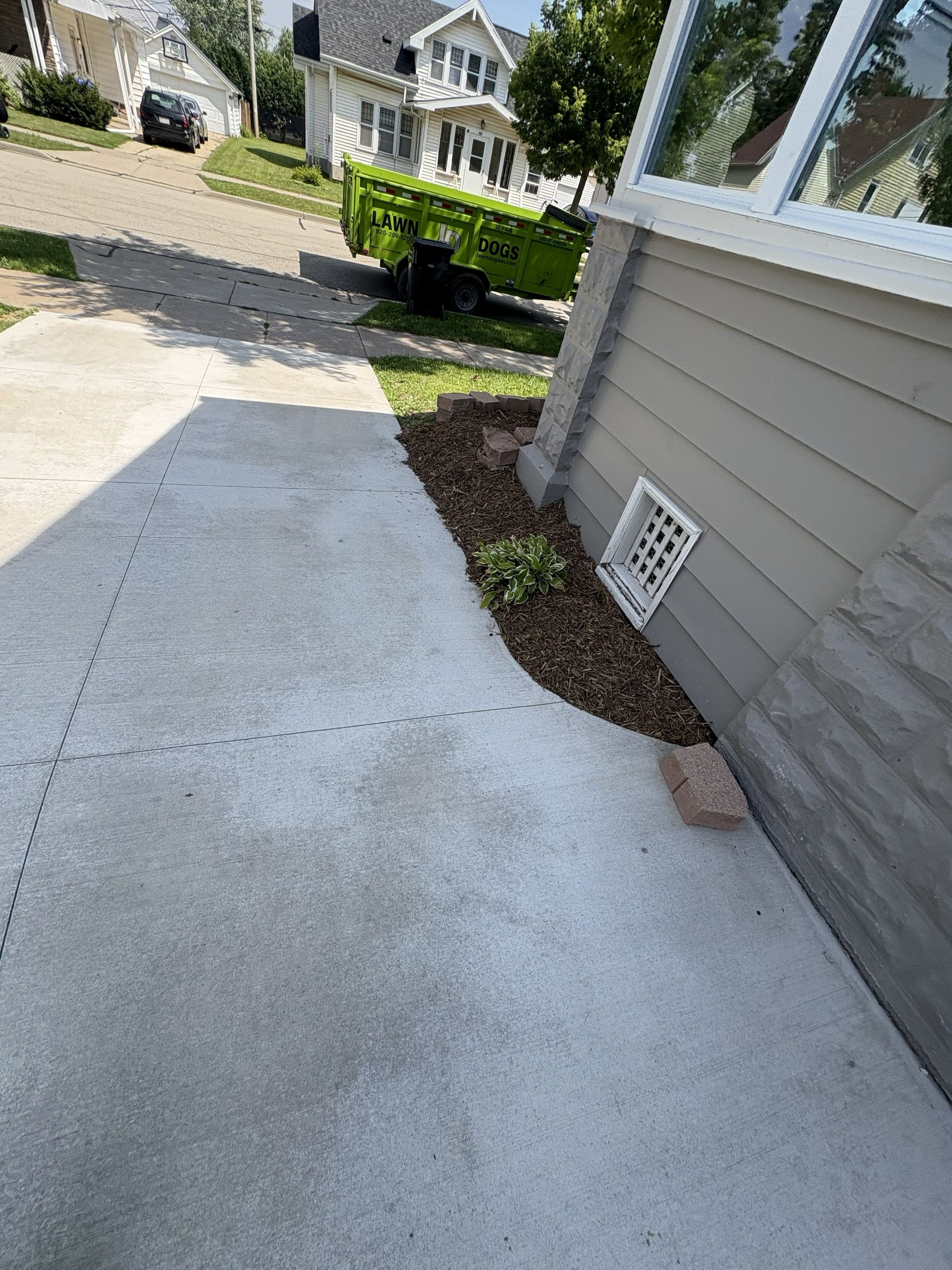 Concrete driveway next to a house with a small planted bed mulched with wood chips.