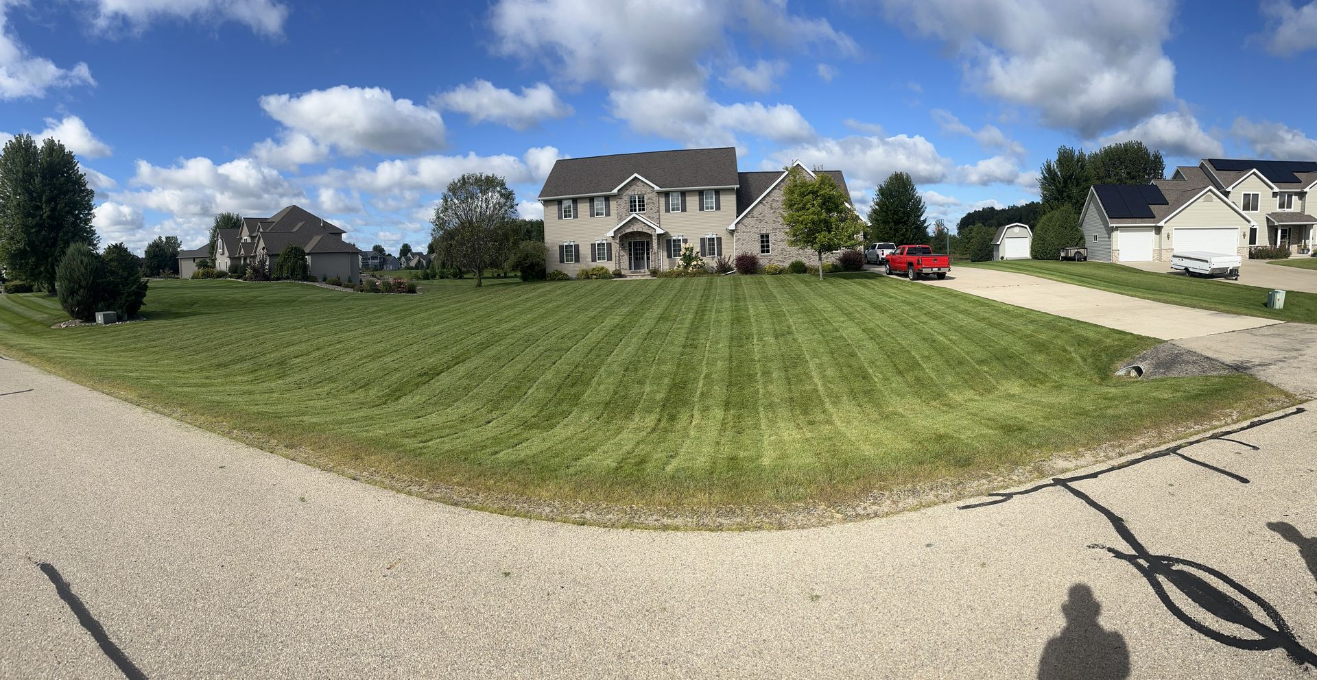 Large, well-kept house with manicured lawn. Cloudy blue sky. Suburban setting with a red truck.