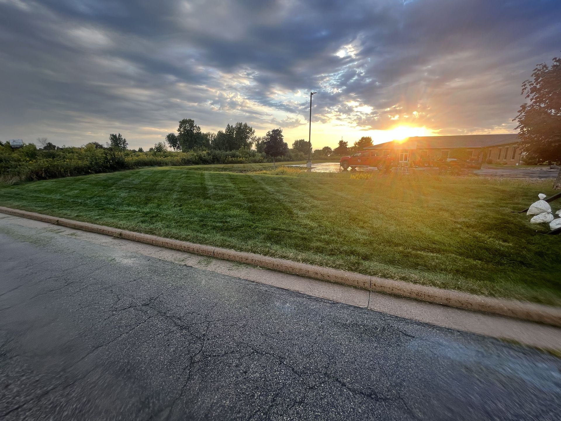 Green grassy field with a setting sun, dark sky, and a road in the foreground.