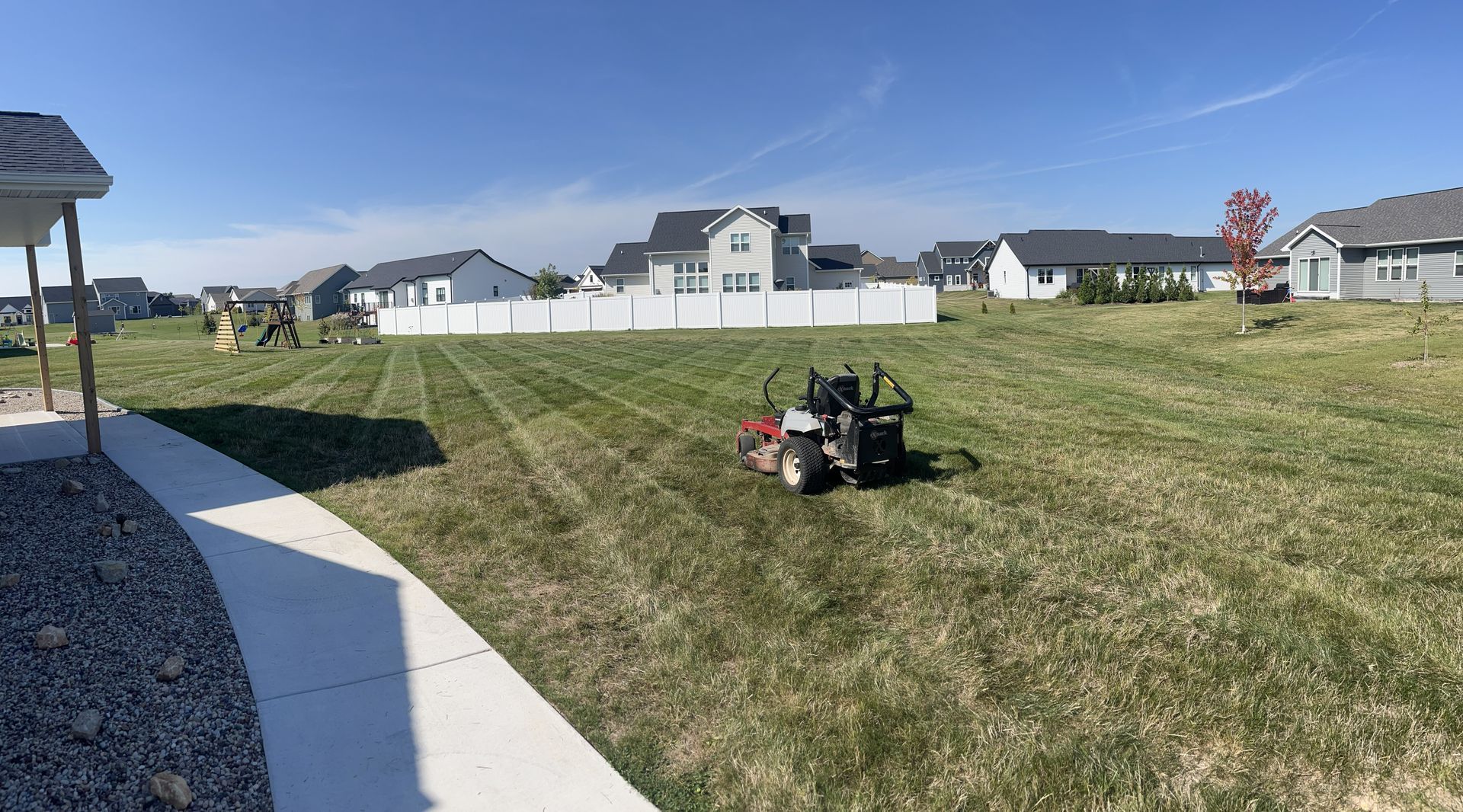 A riding lawnmower cuts grass in a neighborhood yard on a sunny day.